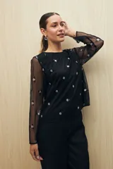 Blusa negra de tul bordado con pequeñas lentejuelas y mangas largas transparentes.