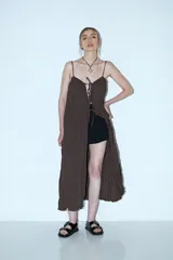 Vestido largo marrón oscuro, con tirantes finos y escote pronunciado que se ajusta con cordones en el centro. El tejido es arrugado o plisado.