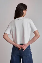 Remera blanca de algodón con cuello redondo y mangas cortas. Presenta apliques de strass en los laterales del ruedo.