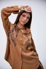 Camisa marrón de manga larga con detalles de lentejuelas y bordados en el frente. Tiene cuello clásico y botones frontales.
