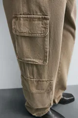 Pantalón de denim color beige, corte relaxed fit, con bolsillos laterales tipo cargo con solapa y cierre de botón. Cierre frontal con botón y cremallera.