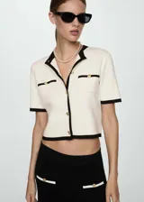 Cárdigan negro de punto fino con cuello redondo y manga corta. Presenta cierre frontal con botones dorados, ribetes blancos en contraste y dos bolsillos de ribete delanteros.