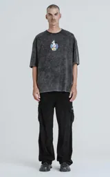 Remera de algodón premium color gris oscuro con efecto nevado (acid wash), corte oversize y manga corta. Estampa trasera con el personaje de Mickey Mouse vestido de chef rodeado de llamas y utensilios de cocina, con texto en inglés y chino.