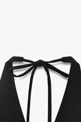 Vestido corto negro con cuello halter y lazada. Tiene bolsillos laterales ocultos y forro interior combinado. El cierre es en la espalda con cremallera oculta.