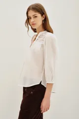 Camisa de algodón color celeste, con escote en V, cierre parcial de botones y detalles de encaje en los hombros. Mangas largas abullonadas con puños elásticos.