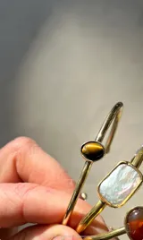 Pulsera rígida dorada con piedra ojo de tigre ovalada engarzada.