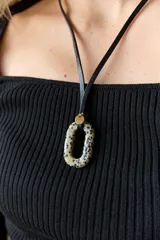 Collar con doble tira de tiento negro, una ajustada al cuello como choker y otra más larga con un dije ovalado de piedra natural blanca y un pequeño detalle dorado.