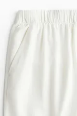 Pantalón culotte color blanco hueso, de tiro alto con cintura elástica, corte amplio y bolsillos laterales.