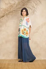 Camisa de manga corta con cuello clásico y cierre frontal con botones. Presenta un estampado con motivos florales, frutales y paisajes.