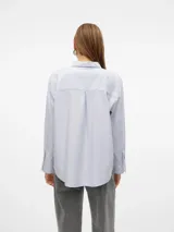 Camisa celeste de corte oversize, con cuello clásico, cierre frontal con botones, bolsillo en el pecho y mangas largas con puños abotonados.