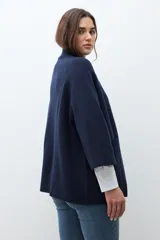 Chaqueta tejida de punto color verde oliva, con cuello alto y cierre frontal de botones a presión. Presenta bolsillos delanteros aplicados y mangas amplias de largo tres cuartos.