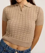 Blusa color beige de tejido de punto con textura cuadriculada, corte crop, cuello polo con cierre de botones y mangas cortas ajustadas.