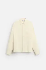 Camisa color crema de corte relaxed fit, confeccionada en tejido con mezcla de viscosa. Tiene cuello solapa, manga larga con puños abotonados, bolsillo de parche en el pecho y cierre frontal con botones.
