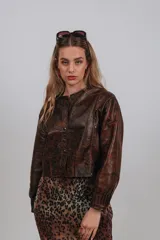 Campera bomber color beige de cuero, con cuello redondo, cierre frontal con botones a presión, mangas largas con puños elásticos y detalles de tachas metálicas en hombros y espalda.