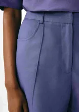 Short de vestir color lila, de corte recto, con bolsillos laterales y cierre frontal con botón y cremallera.