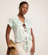Camisa blanca con estampado floral en tonos verdes, de manga corta, cuello camisero y escote en pico. Tiene cierre con botones y lazo en el bajo.