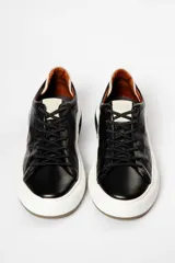Zapatillas urbanas de cuero negro con cordones, suela blanca y detalles en marrón.