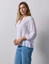 Blusa blanca de gasa bambula con cuello a la base y apertura central con botones. Apliques de crochet en la parte delantera y en las mangas ¾ con terminación fruncida.