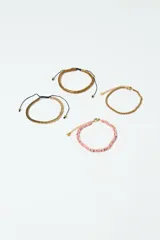 Set de cuatro pulseras: una dorada de cadena, una rosa de cuentas, una dorada tejida con cordón negro ajustable y una dorada con textura y cordón negro ajustable.