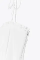 Vestido midi blanco de popelín con escote corazón y volantes. Tiene tirantes finos con detalle de lazo, forro interior combinado y cierre lateral con cremallera oculta.