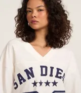 Remera blanca de algodón con cuello en V y corte amplio. Estampado frontal con la inscripción "San Diego", el número 96 y cinco estrellas. Estilo deportivo americano.