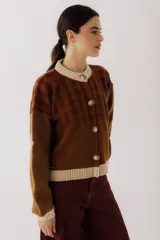 Cárdigan marrón con diseño de rombos en tonos rojizos y beige. Tiene cuello redondo, cierre frontal con botones y mangas largas con puños acanalados.