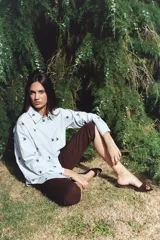 Camisa negra con bordado de flores rosas, corte recto, cuello clásico y cierre frontal con botones.