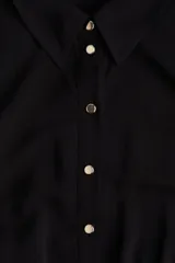 Vestido midi negro con cuello camisero, mangas cortas tipo raglán y botonadura frontal. Presenta elástico en la cintura y cinturón extraíble para atar.