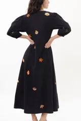 Vestido midi color arena con escote en V, mangas 3/4 abullonadas y cierre frontal con botones. Presenta bordados de motivos marinos.