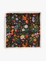 Pañuelo cuadrado de seda con estampado floral multicolor sobre fondo negro y borde liso color crema.