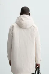 Parka color crudo de tejido técnico acolchado, con cuello alto y capucha ajustable. Tiene mangas largas con puños ajustables, bolsillos frontales con solapa, bolsillo interior y cierre frontal con cremallera oculta por solapa con botones a presión.