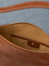 Cartera hobo color marrón confeccionada en cuero vacuno flor, con acceso mediante cierre superior y correa regulable con hebillas metálicas.