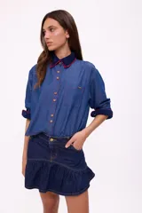 Camisa de denim azul con cuello y puños con detalles de crochet en azul marino y rojo.