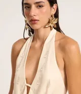 Blusa de crepé color crema, con escote drapeado y espalda descubierta. Presenta aplicaciones de piedras en el frente.