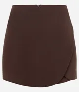 Short pollera corto de sastrería en color bordó, con diseño cruzado de borde redondeado y cierre de cremallera en la parte posterior.