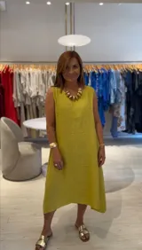 Vestido midi color mostaza confeccionado en lino, de corte acampanado, escote redondo, sin mangas y con bolsillos laterales.