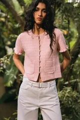 Chaqueta de punto color crema con cuello redondo, manga corta con volantes, bolsillos de plastrón y cierre frontal con botones metálicos.