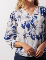 Blusa de gasa estampada con flores azules y blancas, marca Sioni. Tiene escote en V, abertura frontal con botones y mangas 3/4 con puños fruncidos y botón.