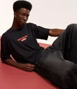 Remera negra de algodón con estampa de duraznos y texto "Bieber's Peaches" en color naranja.