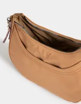 Bandolera hobo negra de tela deportiva con correa regulable, cierre superior, bolsillo frontal y charm lateral decorativo.