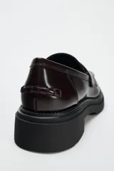 Zapato plano tipo mocasín color borgoña de cuero charol, con detalle de pasados en la parte delantera, copete subido, antifaz y acabado en punta redondeada.