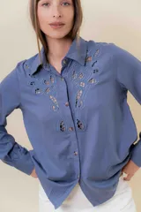 Camisa de manga larga color bordó oscuro, con cuello clásico y bordado calado decorativo en el área del pecho y hombros. Presenta un calce relajado y cierre frontal de botones.