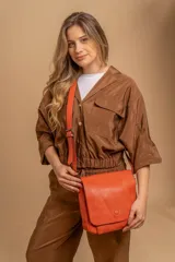 Bandolera de símil cuero color naranja vibrante, con solapa frontal que se cierra con un botón a presión central. Posee una correa ajustable para llevar al hombro o cruzada.