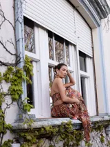 Vestido largo de fiesta con estampado floral en tonos marrones, naranjas y azules. Tiene un top tipo pañuelo con espalda descubierta y falda amplia con abertura lateral.
