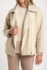 Campera de abrigo color crema, con cuello solapa y cierre frontal asimétrico. Presenta textura bouclé o de lana rizada.