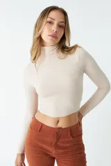 Polera color beige de corte crop, cuello alto y mangas largas.