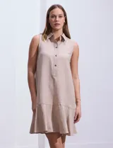 Vestido corto color beige, de corte recto, sin mangas, con cuello camisero, abotonadura frontal y ruedo con volantes.