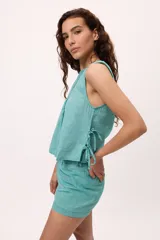 Musculosa blanca de algodón y lino, con tablas verticales en el frente y lazos laterales para regular el ajuste.