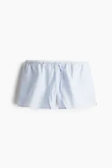 Short de popelina de algodón a rayas verticales celestes y blancas. Tiene cintura elástica con cordón ajustable, bolsillos laterales y aberturas laterales cortas en el bajo.