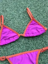 Bikini de dos piezas color fucsia con bordes en naranja. El corpiño es triangular con tirantes finos y la bombacha es colaless regulable con tiras finas laterales.